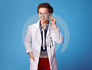 Smiling medical practitioner woman using handsfree on blue