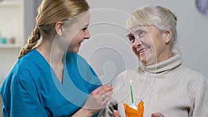 Smiling medical worker bringing muffin with candle to happy senior woman, b-day