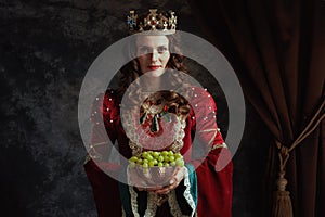 smiling medieval queen in red dress with plate of grapes