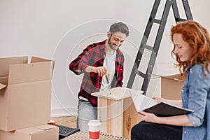 Smiling man folding furniture while woman unpacking stuff after relocation