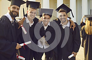 Smiling men students university graduates standing, hugging and celebrating getting diplomas