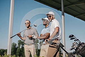 Smiling men in sunglasses holding golf clubs outdoors