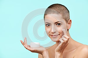 Smiling mid 30s woman applying moisturizing cream on her face. Photo of attractive caucasian woman with healthy skin.