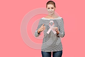 Smiling mid 30s woman, a cancer survivor, holding pink breast cancer awareness ribbon and showing thumbs up.