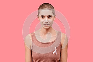 Smiling mid 30s woman, a cancer survivor, wearing pink breast cancer awareness ribbon, isolated over living coral background.