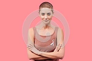 Smiling mid 30s woman, a cancer survivor, wearing pink breast cancer awareness ribbon, isolated over living coral background.