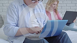 Smiling mid-adult man using social media on laptop and smiling with blurred senior woman surfing Internet at the