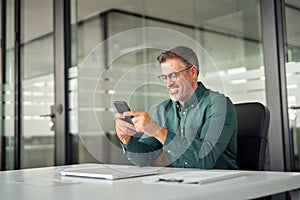 Smiling mid aged business man using cell phone at work desk.