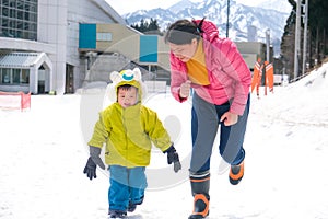 Smiling middle age Asian Mother and cute smiling little 2-3 years old toddler boy child playing happily in snow