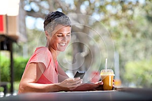 Smiling middle age woman sitting outside with mobile phone and drink