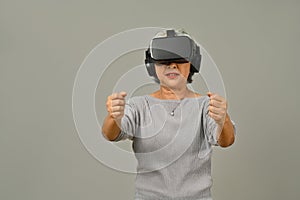 Smiling middle age woman with virtual reality glasses simulating of driving car in VR glasses isolated on gray
