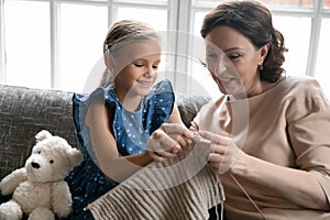 Smiling middle aged 50s grandmother teaching interested small granddaughter knitting.