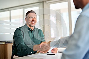 Smiling middle aged business man handshaking partner at office meeting.