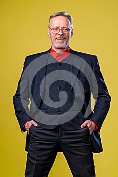 Smiling middle aged business man isolated on yellow with hands in pants pockets. Vertical Format standing