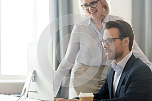 Smiling middle-aged businesswoman help male employee working on pc