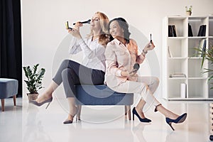 Smiling middle aged businesswomen sitting together and applying makeup in office