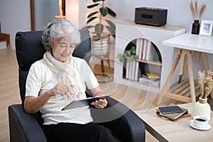 Smiling middle-aged Caucasian woman sit on couch in living room browsing wireless Internet on tablet