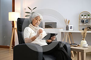 Smiling middle-aged Caucasian woman sit on couch in living room browsing wireless Internet on tablet