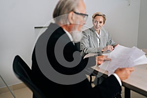 Smiling middle-aged CEO businesswoman in suit looking listening to senior adult executive manager discussing corporation