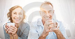 Smiling middle aged couple sitting on the couch having coffee