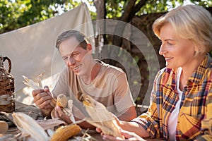 Smiling middle-aged couple sitting at table, shucking corn