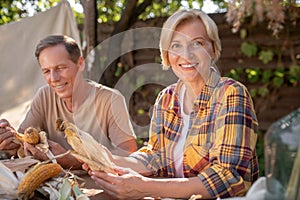 Smiling middle-aged couple sitting at table, shucking corn