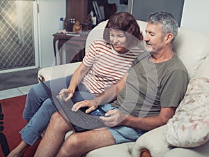 Smiling middle aged couple sitting on their couch using the laptop to buy online at home