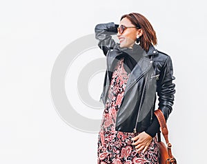 Smiling middle-aged female dressed boho fashion style colorful long dress with black leather biker jacket with brown leather flap