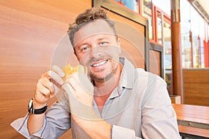 Smiling middle aged man eat an hamburger in fast food