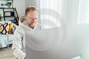 Smiling Middle-aged man in eyeglasses using a modern computer in his living room. Writing or Distance or freelance work on