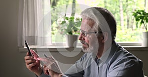 Smiling middle aged man in eyewear using smartphone.