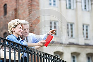 Smiling middle-aged man showing something to woman with guidebook in city photo