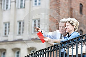 Smiling middle-aged man showing something to woman with guidebook in city photo