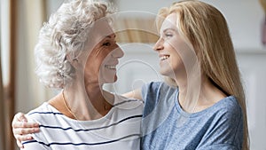 Smiling middle aged mature woman cuddling attractive grown up daughter.