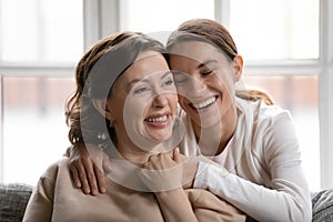 Smiling middle-aged mother and adult daughter hug at home