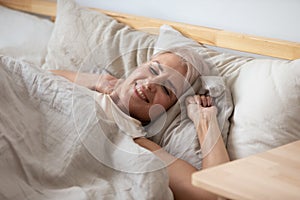 Smiling middle aged retired woman waking up in cozy bed.