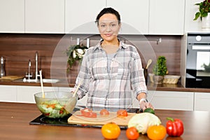 Smiling middle-aged woman in casual shirt preparing lunch in the kitchen