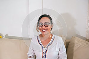 A smiling, middle-aged woman looking at the camera, a happy old lady with glasses posing at home