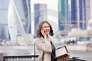 Smiling middle-aged woman with notebook talking on the phone