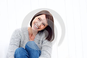 Smiling middle aged woman sitting against white wall