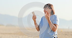 smiling middle aged woman talking on video call using smartphone with headphones on the beach. female 50 years remote