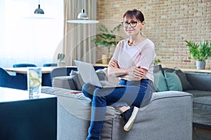 Smiling middle aged woman using laptop, sitting on sofa at home