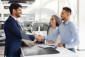 Smiling middle-eastern man and woman buying car at salon