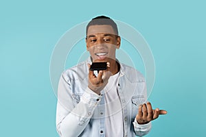 Smiling millennial african american guy in casual calls by smartphone, talk with friend, isolated on blue background
