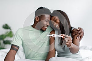 Smiling millennial african american male and female rejoice and show positive pregnancy test in bedroom