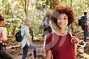 Smiling millennial African American woman hiking in a forest with friends, waist up, close up