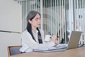 Smiling millennial Asian female office worker working with financial reports for tax audit reports or financial