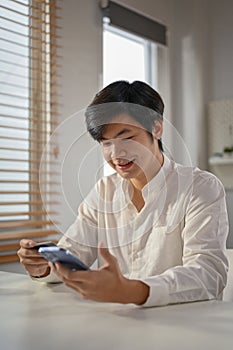 Smiling millennial Asian man using mobile banking application to pay online bills