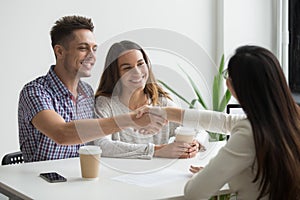 Smiling millennial couple handshaking realtor or advisor making