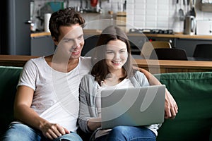 Smiling millennial couple using laptop computer sitting on kitch